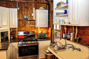 Une cuisine avec des murs en bois, des armoires blanches, une cuisinière, un évier et une fenêtre.