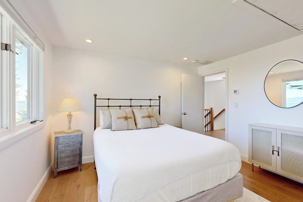 A bedroom with a bed, bedside table, lamp, and a mirror on the wall.