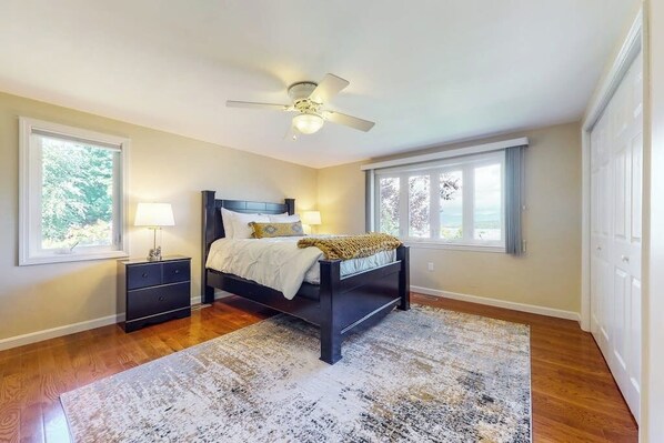 A bedroom with a bed, nightstands, a ceiling fan, and large windows. - 3BR Lakeview - Fireplace - Patio - Firepit (Gilford)