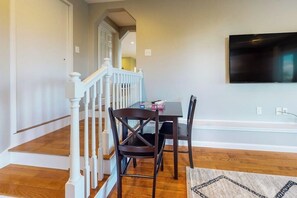 A dining area with a table, chairs, and a television mounted on the wall. - 3BR Lakeview - Fireplace - Patio - Firepit (Gilford)