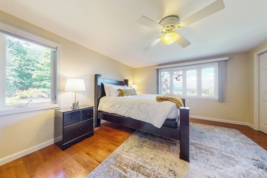 A bedroom with a bed, nightstands, a ceiling fan, and large windows.