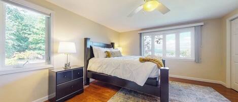 A bedroom with a bed, nightstands, a ceiling fan, and large windows.