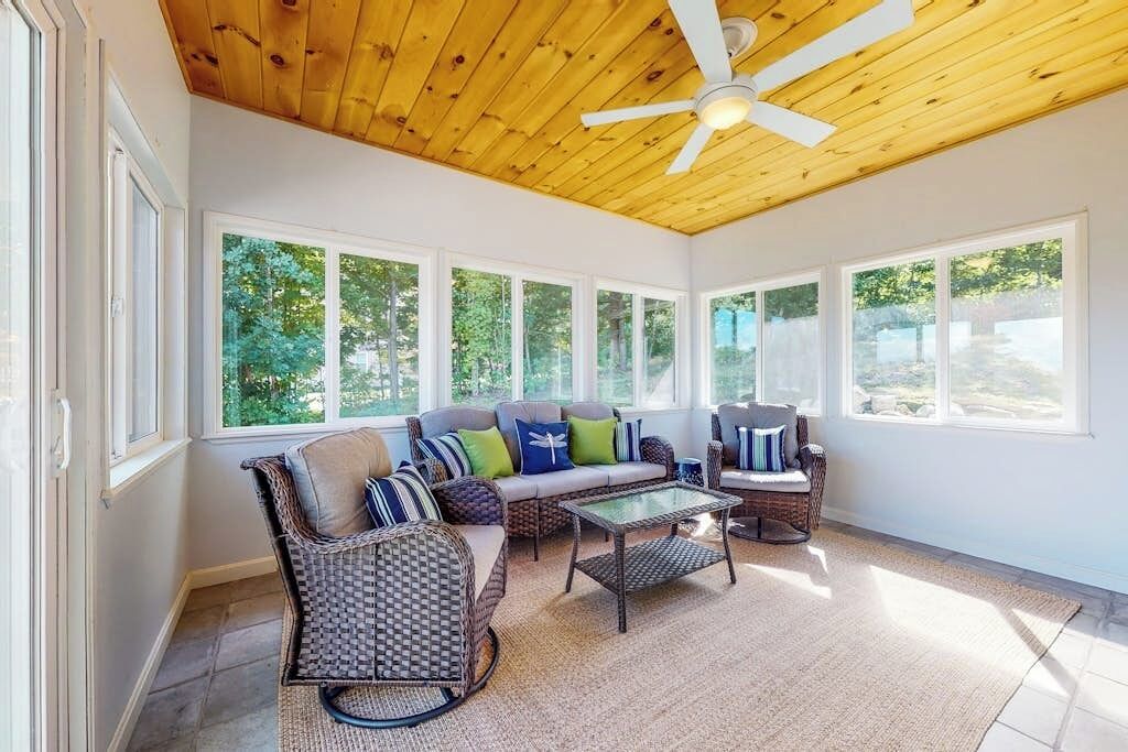 A sunlit room with a ceiling fan, large windows, a sofa, and wicker furniture.