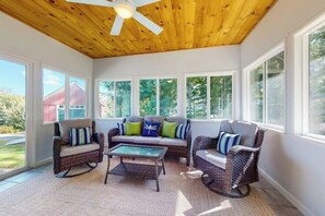 A sunroom with wicker furniture, large windows, and a ceiling fan. - 3BR Lakeview - Fireplace - Patio - Firepit (Gilford)