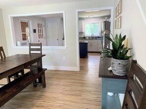 A dining area with a wooden table and chairs, a kitchen with white cabinets, and a potted plant on a counter. - 3BR lakefront home with deck, dock, & game room (Alton)