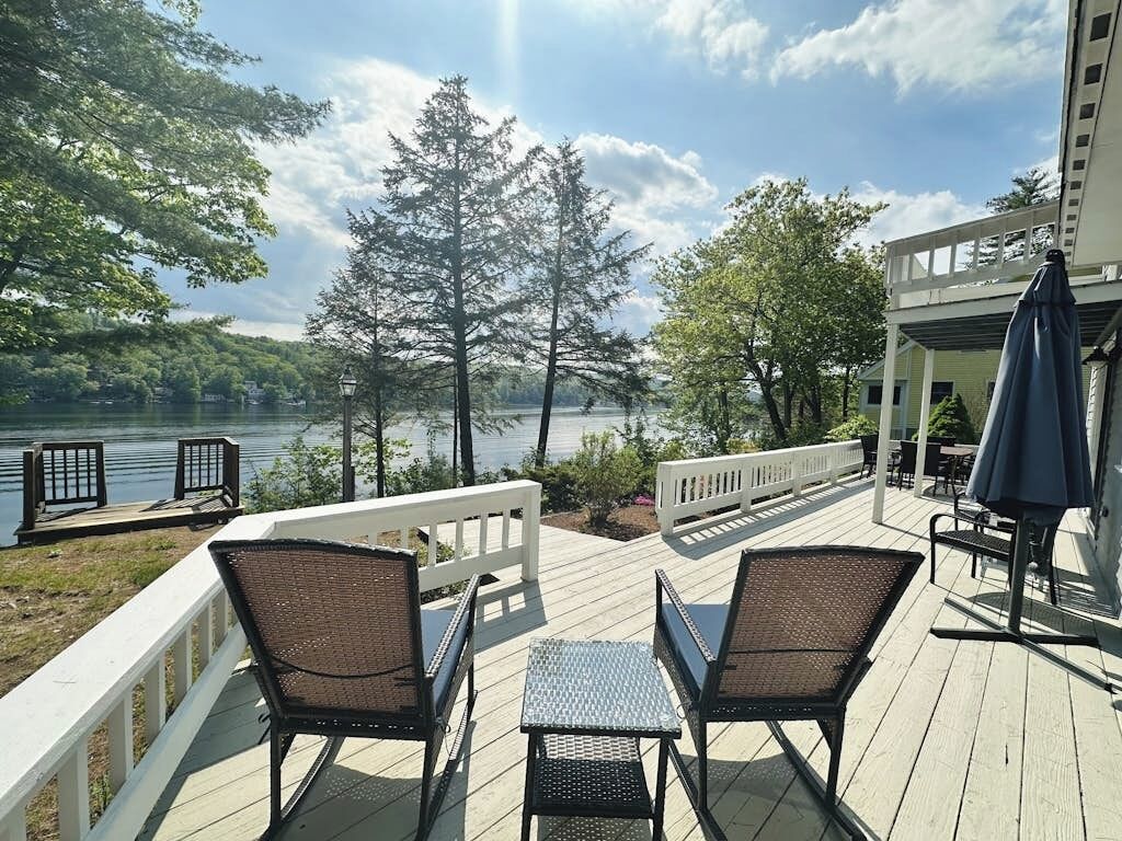 A deck with outdoor seating, overlooking a body of water and trees.