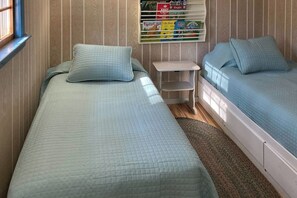 A room with two beds, a small table, and a shelf with books. - 3BR - Dock - Fireplace - Deck - Tennis (Meredith)