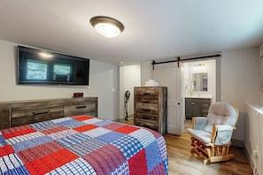 A bedroom with a bed, a chair, a dresser, a TV, and a sliding door leading to a bathroom. - 4BR Beautiful renovated home, centrally Located (Gilford)