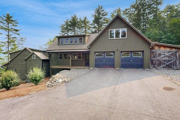 A two-story house with a garage, a covered porch, and a stone retaining wall. - 4BR Beautiful renovated home, centrally Located (Gilford)