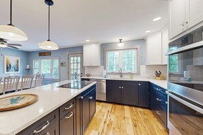 A modern kitchen with a central island, dark cabinetry, and a wooden floor. - 4BR Beautiful renovated home, centrally Located (Gilford)