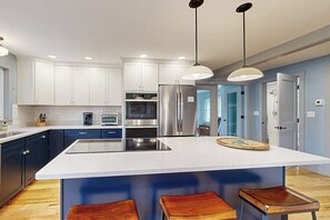 A modern kitchen with white cabinets, stainless steel appliances, and a central island with stools. - 4BR Beautiful renovated home, centrally Located (Gilford)
