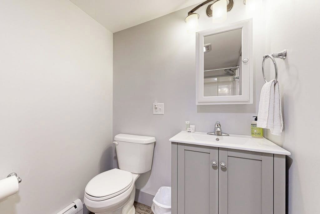 A bathroom with a toilet, sink, mirror, and towel rack.