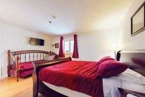 Un dormitorio con una cama doble, un televisor montado en la pared y un ventanal con cortinas.