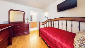 A bedroom with a wooden bed, a dresser, a mirror, and a television on the wall.