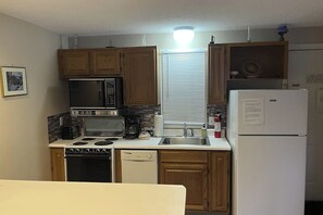 A compact kitchen with wooden cabinets, a microwave, stove, dishwasher, and a refrigerator. - 1 BR condo - Outdoor Pool - Private Beach (Gilford)