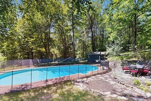 A swimming pool surrounded by a stone deck, with a small building and outdoor seating area in the background. - 3BR stunning home with views, pool & lake access (Meredith)