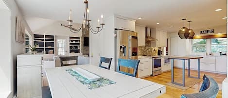 A modern kitchen with white cabinetry, a dining area with a white table, and a chandelier.