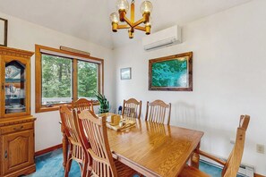 A dining room with a wooden table and chairs, a chandelier, a window with a view of trees, and a painting on the wall. - 3BR withbeach, pool, tennis, game room, porch &views (Gilford)