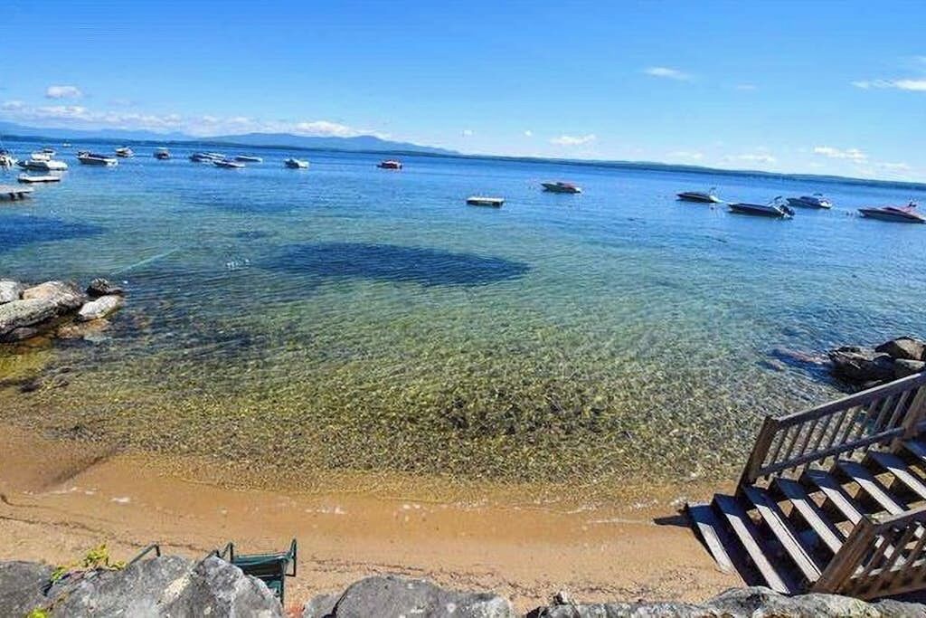 A beach with clear water, boats, and a wooden staircase leading down to the shore.