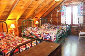 A rustic attic room with wooden beams, multiple beds with colorful quilts, and a window with curtains. - Charming 3BR Lakefront Dog Friendly (Moultonborough)