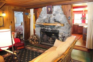 A cozy room with a stone fireplace, a bed with a white comforter, and a wooden floor. - Charming 3BR Lakefront Dog Friendly (Moultonborough)