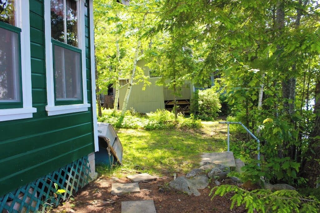 Una casa verde con patio cercado, una terraza de madera y un cobertizo pequeño.