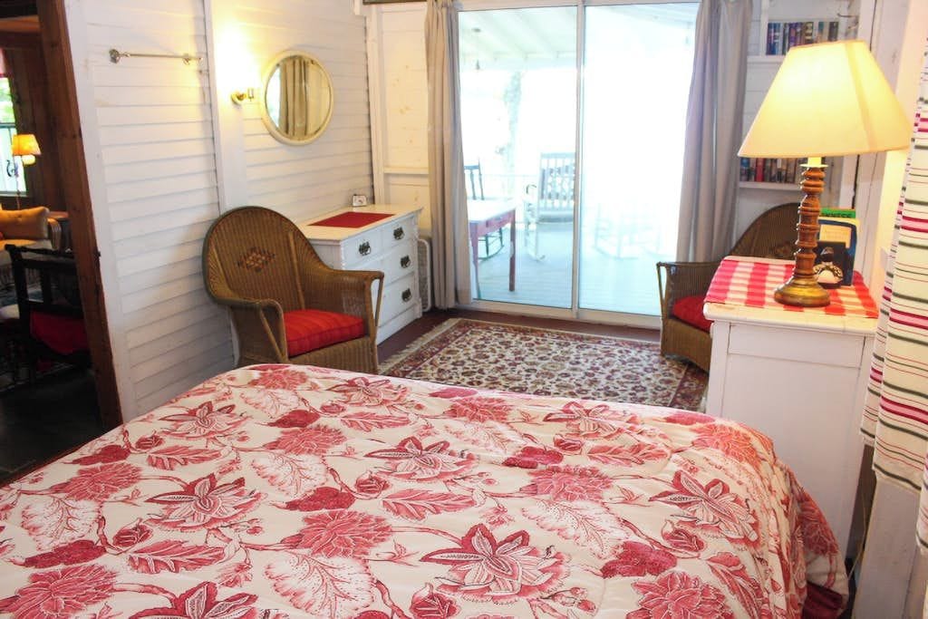 Una habitación con cama, una silla, un escritorio con lámpara, un espejo y vistas al exterior.
