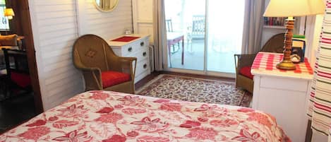 Una habitación con cama, una silla, un escritorio con lámpara, un espejo y vistas al exterior.