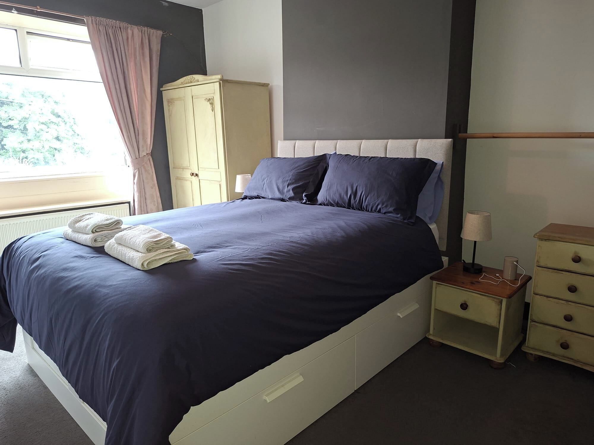 A bedroom with a bed, a nightstand, a dresser, and a window with curtains.