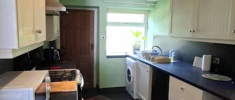 A kitchen with a washing machine, a microwave, and cabinets.