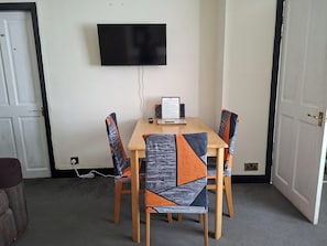 Una habitación con una televisión de pantalla plana montada en la pared, una mesa con sillas y un documento enmarcado sobre la mesa.