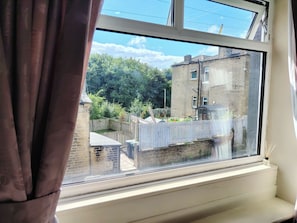 Una ventana con vista a un edificio de ladrillo, una valla de madera y follaje.