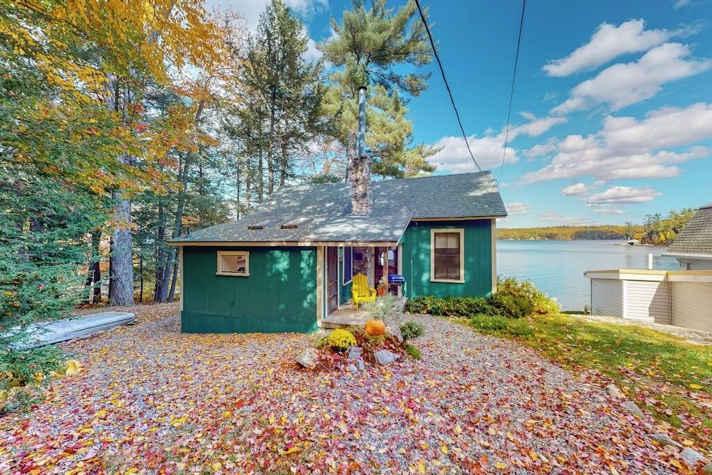 Une maison à l’extérieur vert, avec une cheminée et une véranda où se trouve une chaise.