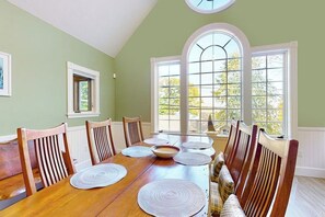 A dining room with a wooden table, chairs, and large windows. - Stunning 2BR Lakefront - Dock - Patio - Washer Dryer (Moultonborough)