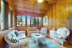 A wooden-paneled room with wicker furniture, large windows, and a ceiling fan. - Stunning 2BR Lakefront - Dock - Patio - Washer Dryer (Moultonborough)