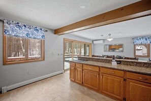 A kitchen with wooden cabinets, a granite countertop, and a window with blue floral curtains. - 3BR home near outdoor rec with deck & games (Gilford)