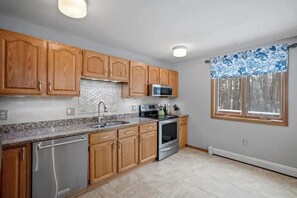 A kitchen with wooden cabinets, a stainless steel dishwasher, a microwave, and an oven. - 3BR home near outdoor rec with deck & games (Gilford)