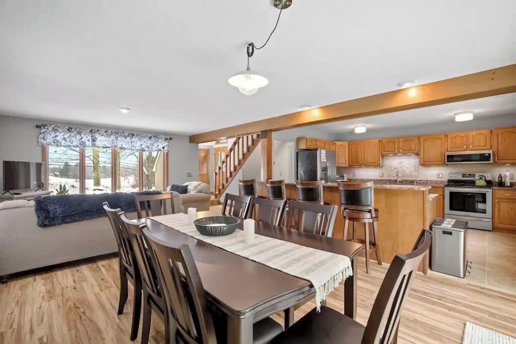 A modern kitchen with wooden cabinets, a dining area with a table and chairs, and a staircase leading to another level.