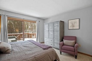A bedroom with a bed, a chair, a wardrobe, and a balcony with a view of trees. - 3BR home near outdoor rec with deck & games (Gilford)