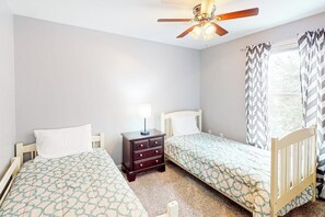 A bedroom with two single beds, a nightstand with a lamp, a ceiling fan, and a window with patterned curtains. - 3BR Mountainview Dog Friendly - Balcony - Washer Dryer (Gilford)
