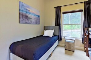 A single bed with a dark blue mattress and white pillow in a room with a window, a radiator, and a bunk bed to the right. - Lake view 2BR with dock & deck, walk to the beach (Moultonborough)