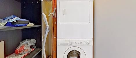 Ein Waschraum mit übereinander gestapelten Waschmaschine und Trockner, Regalen mit Reinigungsmitteln und einem Telefon.