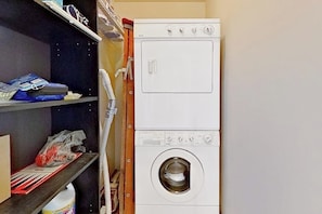 Zona de bugaderia amb una rentadora i una assecadora apilades, prestatges amb productes de neteja i un telèfon.