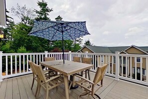 Eine Holzterrasse mit Tisch und Stühlen, einem gemusterten Sonnenschirm und einem weißen Geländer.