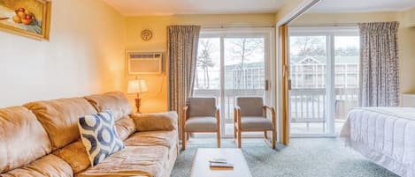 A hotel room with a leather sofa, a wooden coffee table, two armchairs, a bed, and a sliding glass door leading to a balcony.