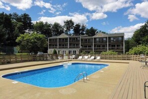 A rectangular swimming pool with a diving board, surrounded by a wooden deck. - 1BR Lakeview 2nd-Floor - Balcony - Outdoor Pool (Gilford)