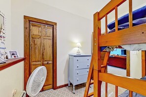 Ein Zimmer mit einem Etagenbett, einem Holzschrank, einem Schminktisch und einem Ventilator sowie einer Lampe.