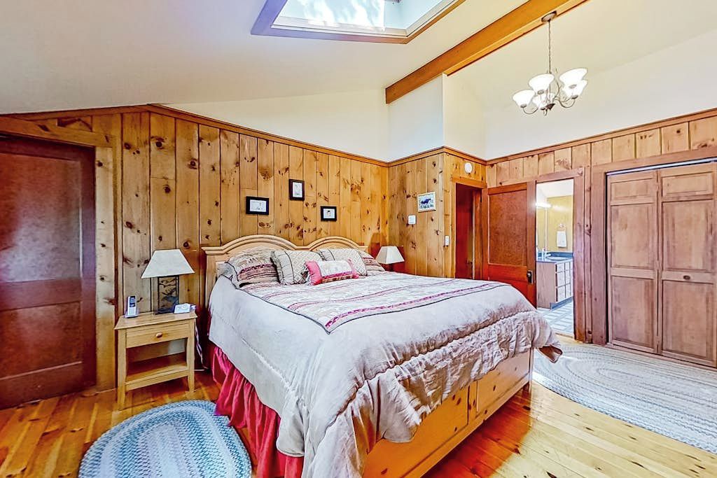 Ein Schlafzimmer mit einem hölzernen Kopfteil, einem Bett mit weißer und pinkfarbener Bettdecke, einem Nachttisch mit Lampe und einem Oberlicht über dem Bett.