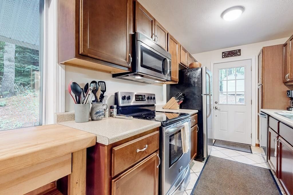 A kitchen with wooden cabinets, a microwave, stove, and a refrigerator.