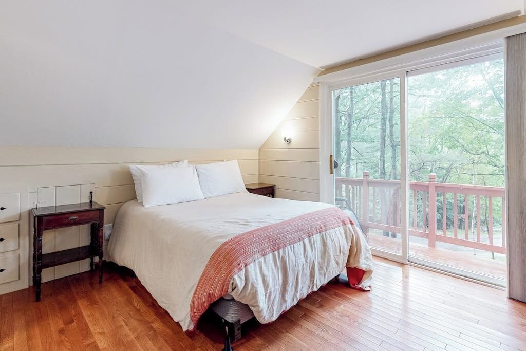 A bedroom with a bed, a nightstand, a window, and a view of trees.
